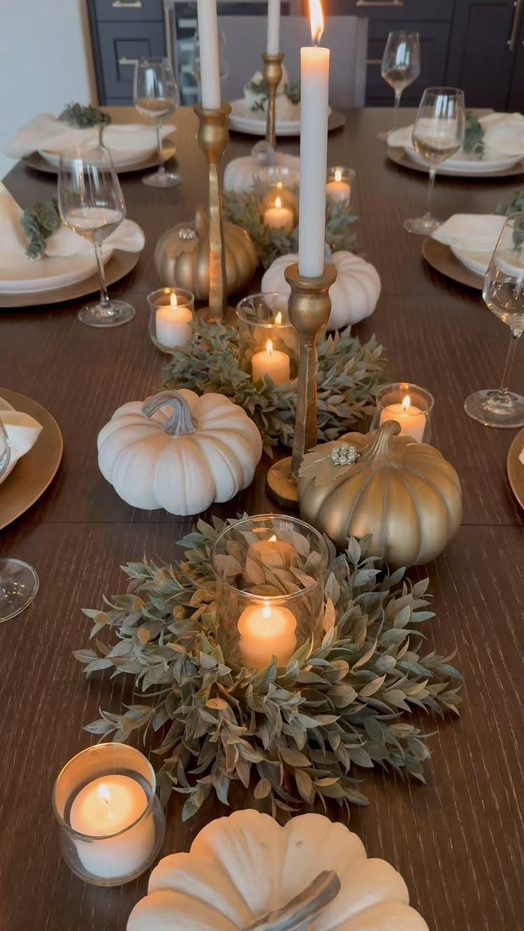 Dining table set with white and gold pumpkins, candles, and green foliage wreaths.