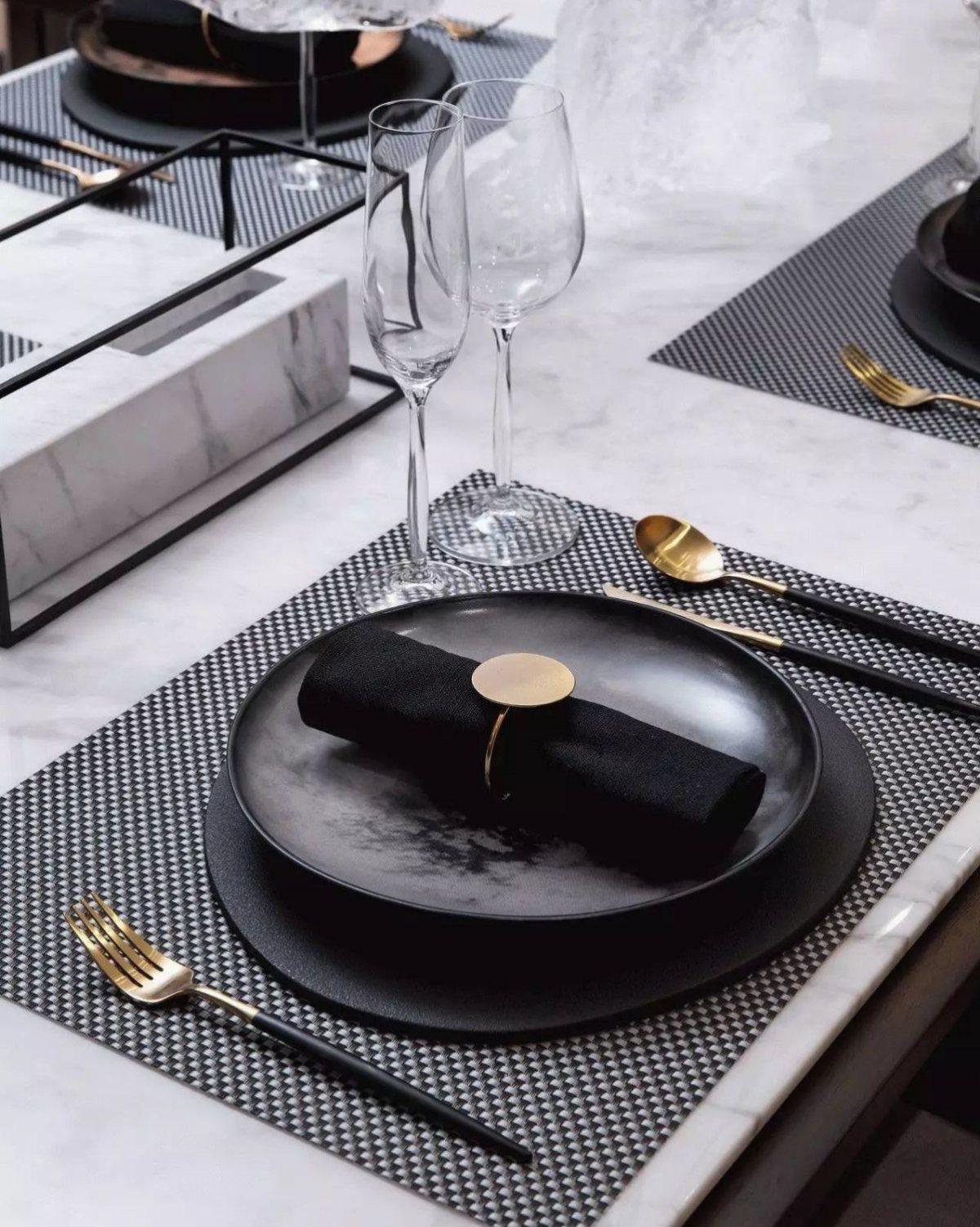 Modern black and gold table setting with plates and glassware on marble surface