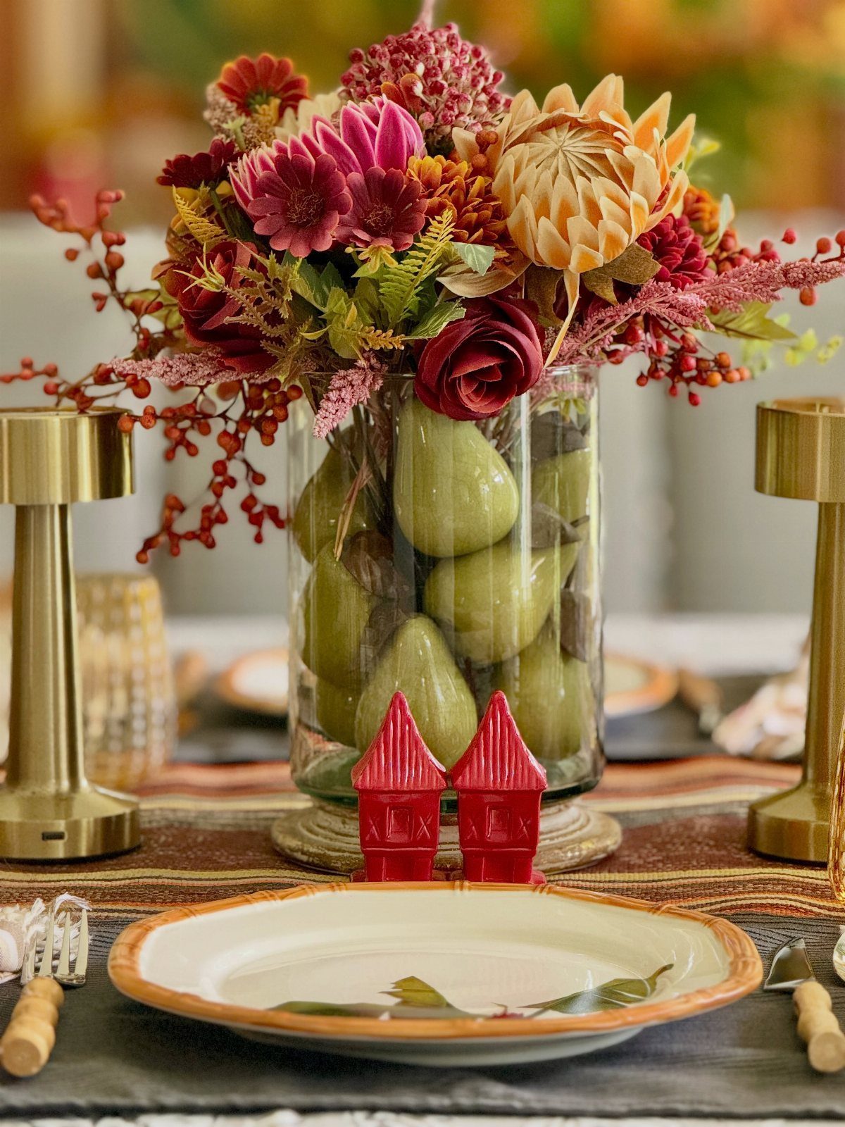 Glass vase filled with green pears topped with autumn flowers on a table.