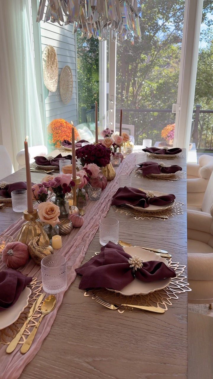 Elegant dining table setting with burgundy napkins, gold accents, and pink floral centerpieces.