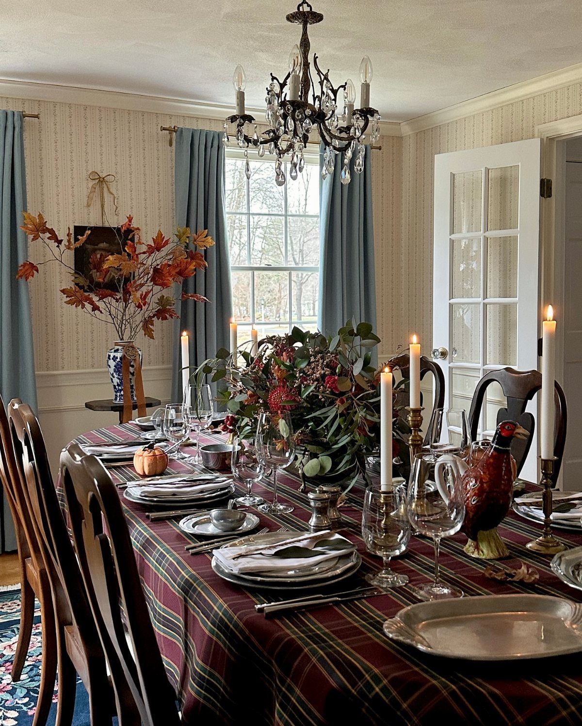 Formal dining table with plaid tablecloth, autumn floral centerpiece, and white taper candles.