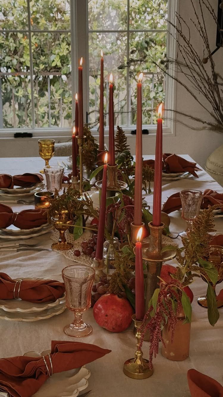 Autumnal dinner table setting with red taper candles, pomegranates, and red napkins.