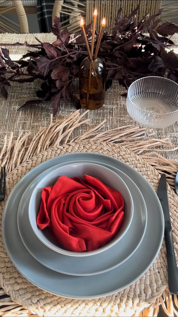 Grey plates and a red rose-folded napkin on a woven placemat with autumn foliage.