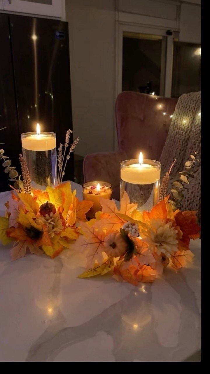 Autumn table setting with lit candles, orange fall leaves, and dried floral sprigs.