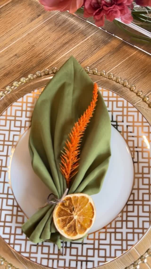 Olive green napkin with dried orange slice and sprig on a gold charger plate