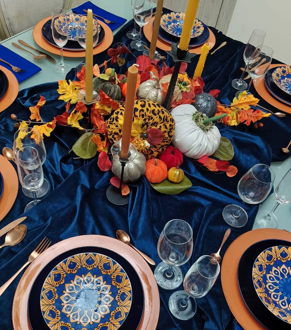 Indigo velvet table setting with blue patterned plates, gold flatware, and autumn pumpkins.