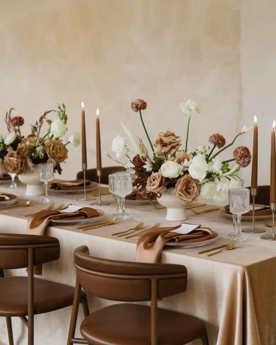 Elegant dining table with beige linen, gold flatware, and autumn floral centerpieces.