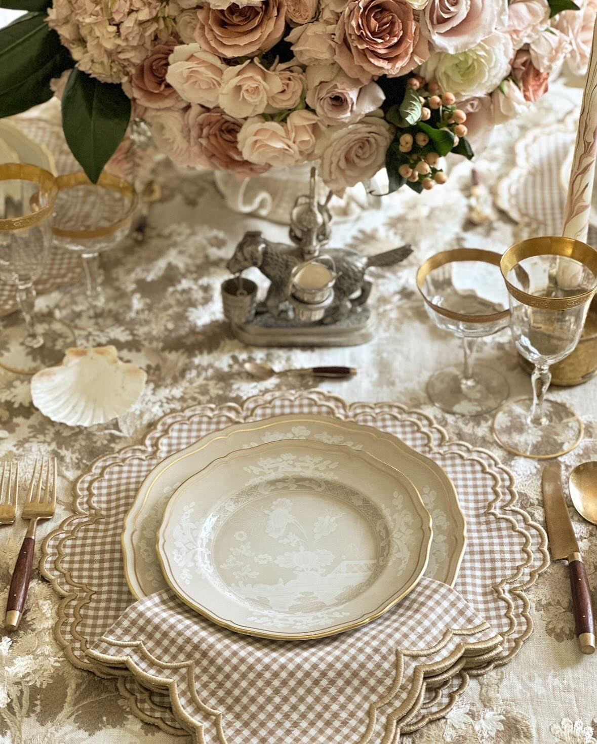 Elegant table setting with gold-rimmed plates, glassware, and roses on lace tablecloth.