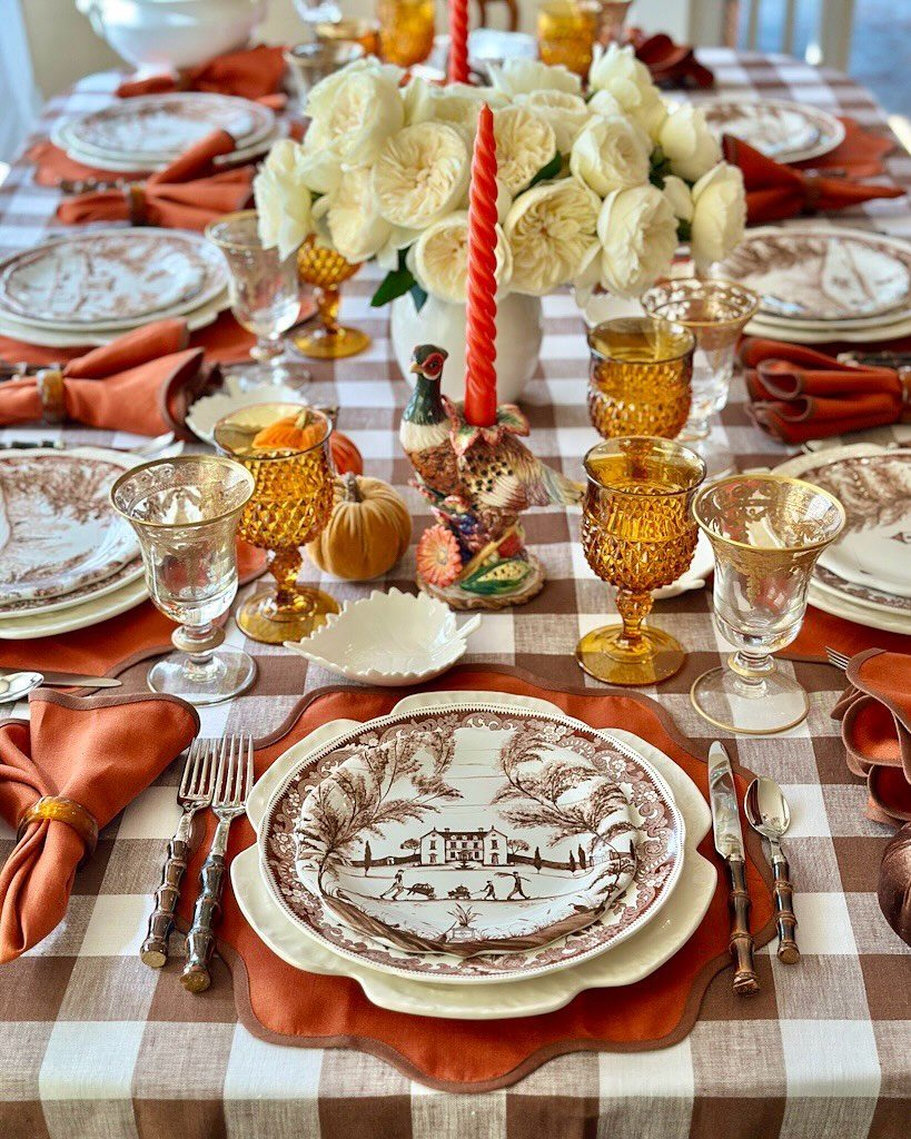 Elegant Thanksgiving table with checkered cloth, orange napkins, and white floral centerpiece.