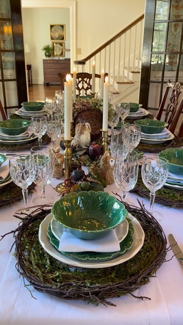 Elegant dining table with green bowls, crystal glasses, and a mossy twig centerpiece.