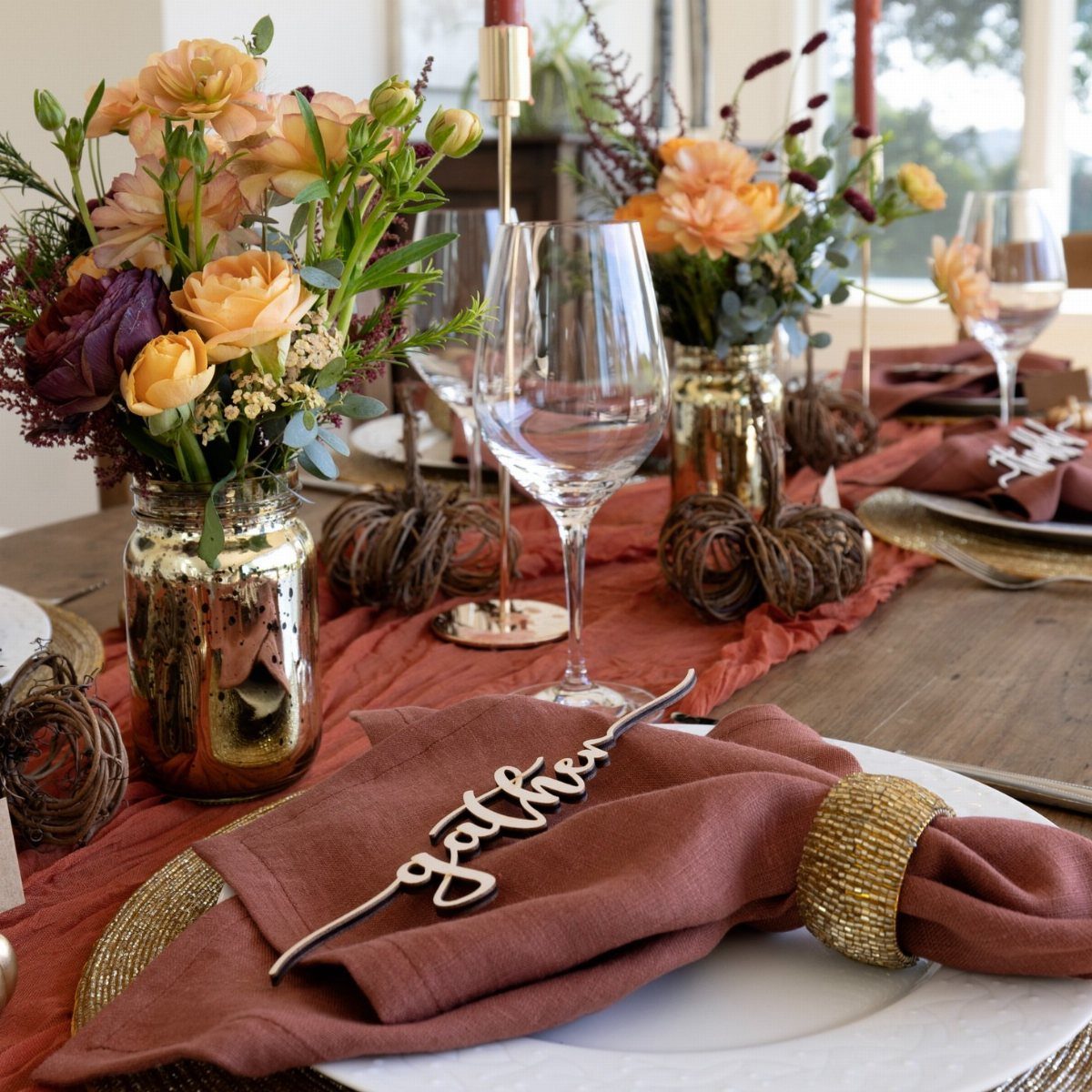Elegant Thanksgiving table setting with terracotta runner, orange flowers, and gold accents.