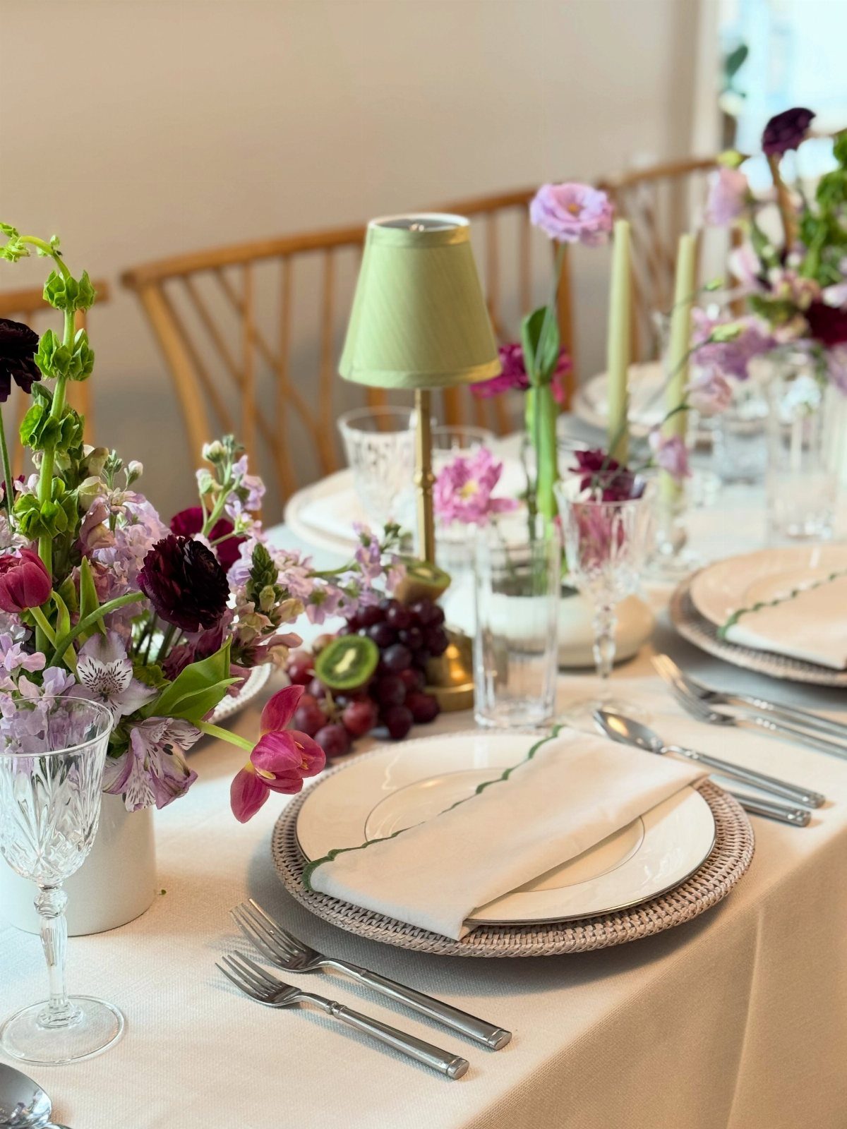 Elegant table setting with purple flowers, red grapes, and white dinnerware on a tablecloth.