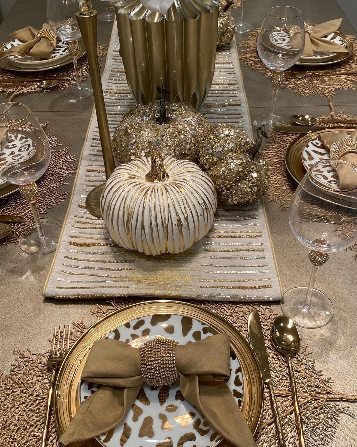 Gold flatware and leopard print plates with gold glittery pumpkins on a table.