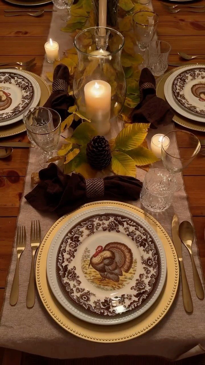 Thanksgiving table setting with turkey plates, gold chargers, and glass candle holders.