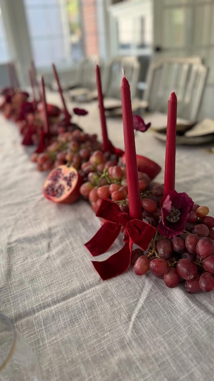 Burgundy taper candles and red grapes on a grey linen dining table centerpiece