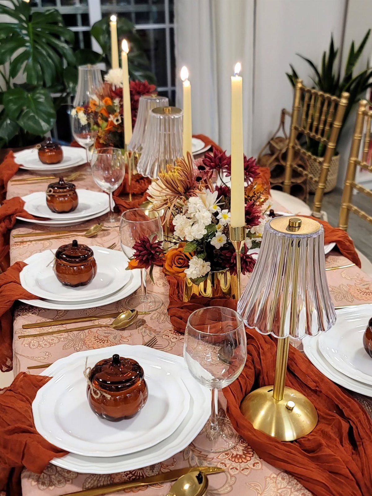 Elegant Thanksgiving table with white plates, orange runners, gold flatware, and autumn florals.