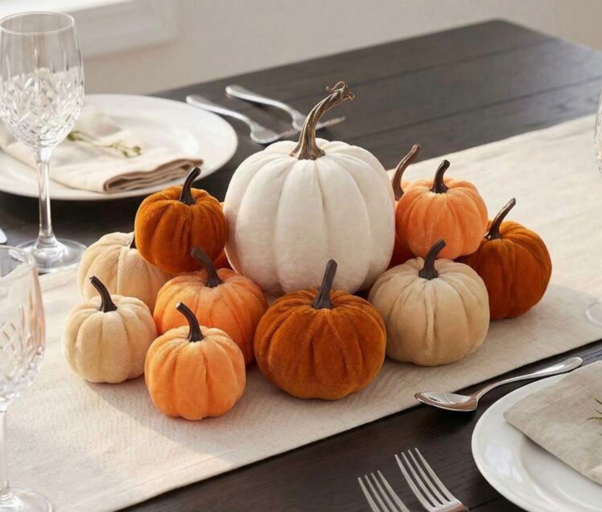 Velvet pumpkins in autumn colors arranged on a light table runner with dinnerware.