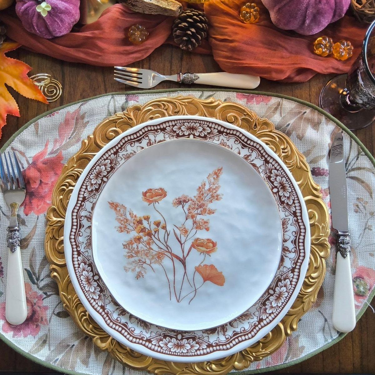 Floral white plate on a gold charger with autumnal pumpkins and fabric decor.