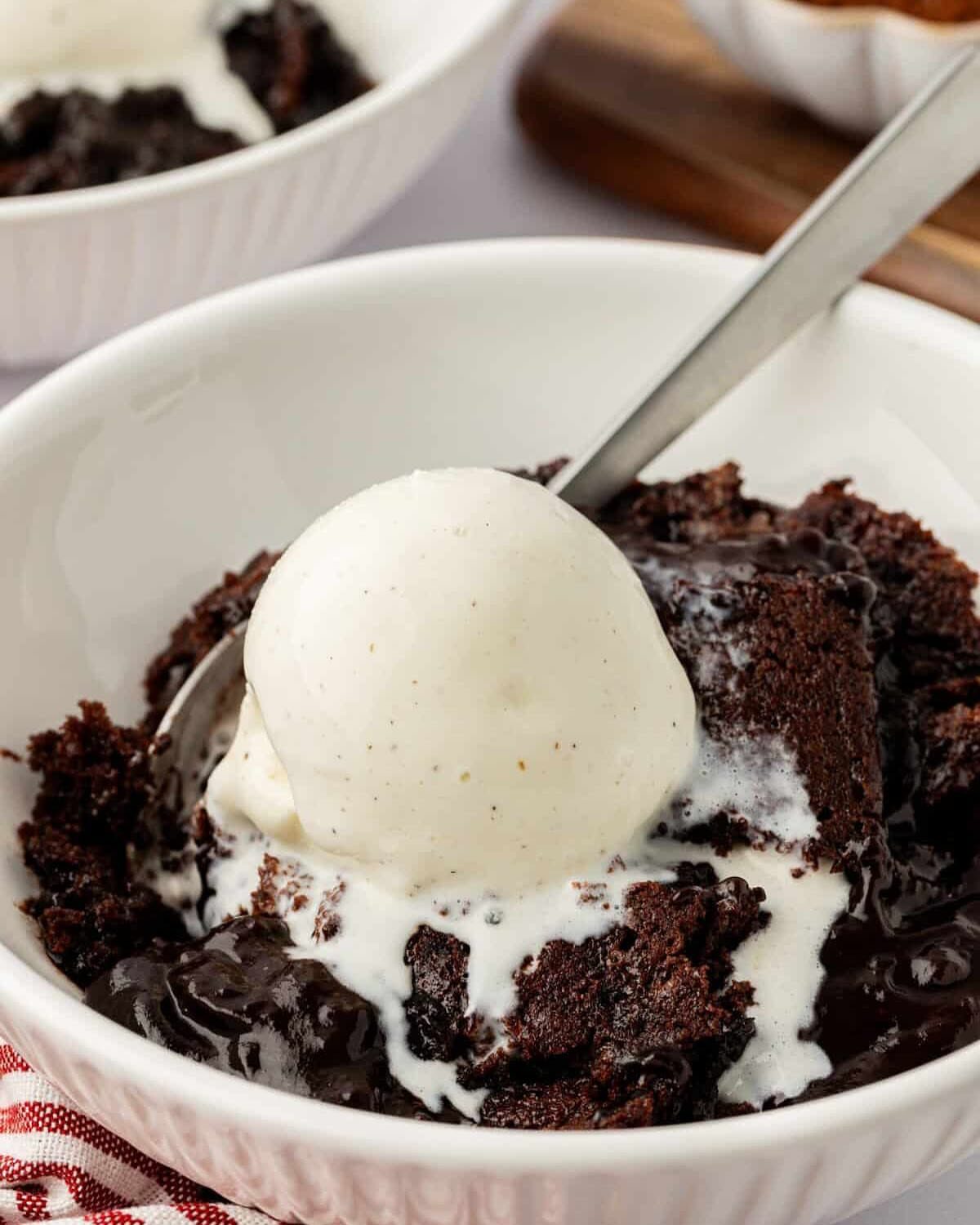 Chocolate cobbler topped with a scoop of melting vanilla ice cream in a white bowl