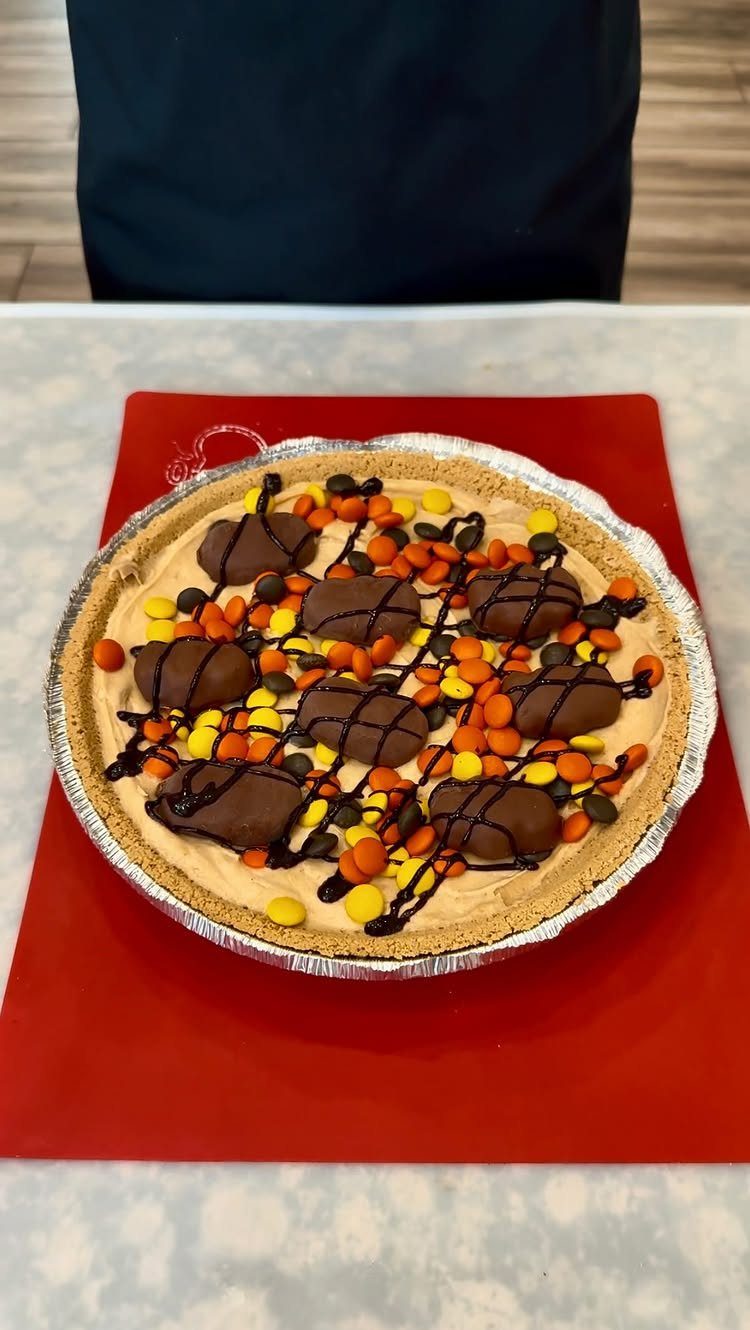Peanut butter pie topped with chocolate peanut butter cups and colorful candy pieces.