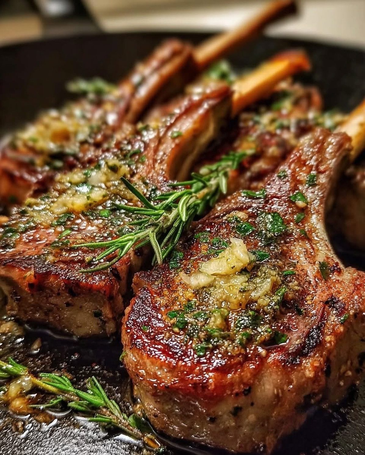 Grilled lamb chops topped with garlic, herbs, and fresh rosemary in a pan.