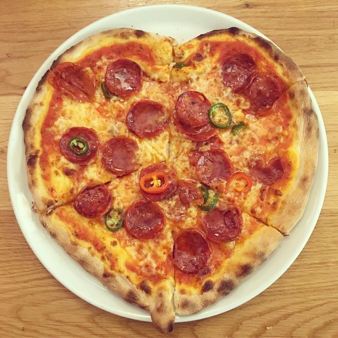 Heart-shaped pepperoni pizza with peppers on a white plate over a wooden table.