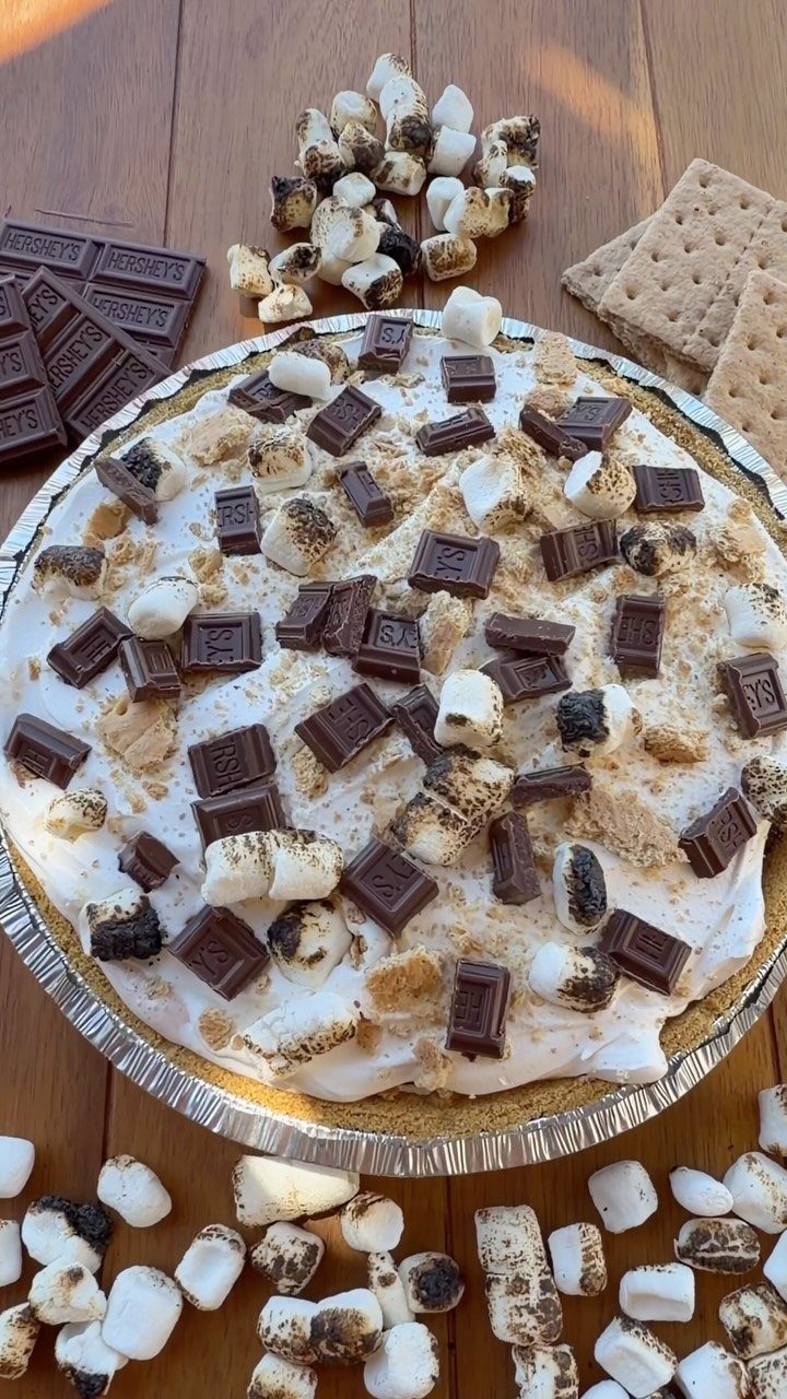 S'mores pudding pie topped with toasted marshmallows and chocolate on a wooden table.