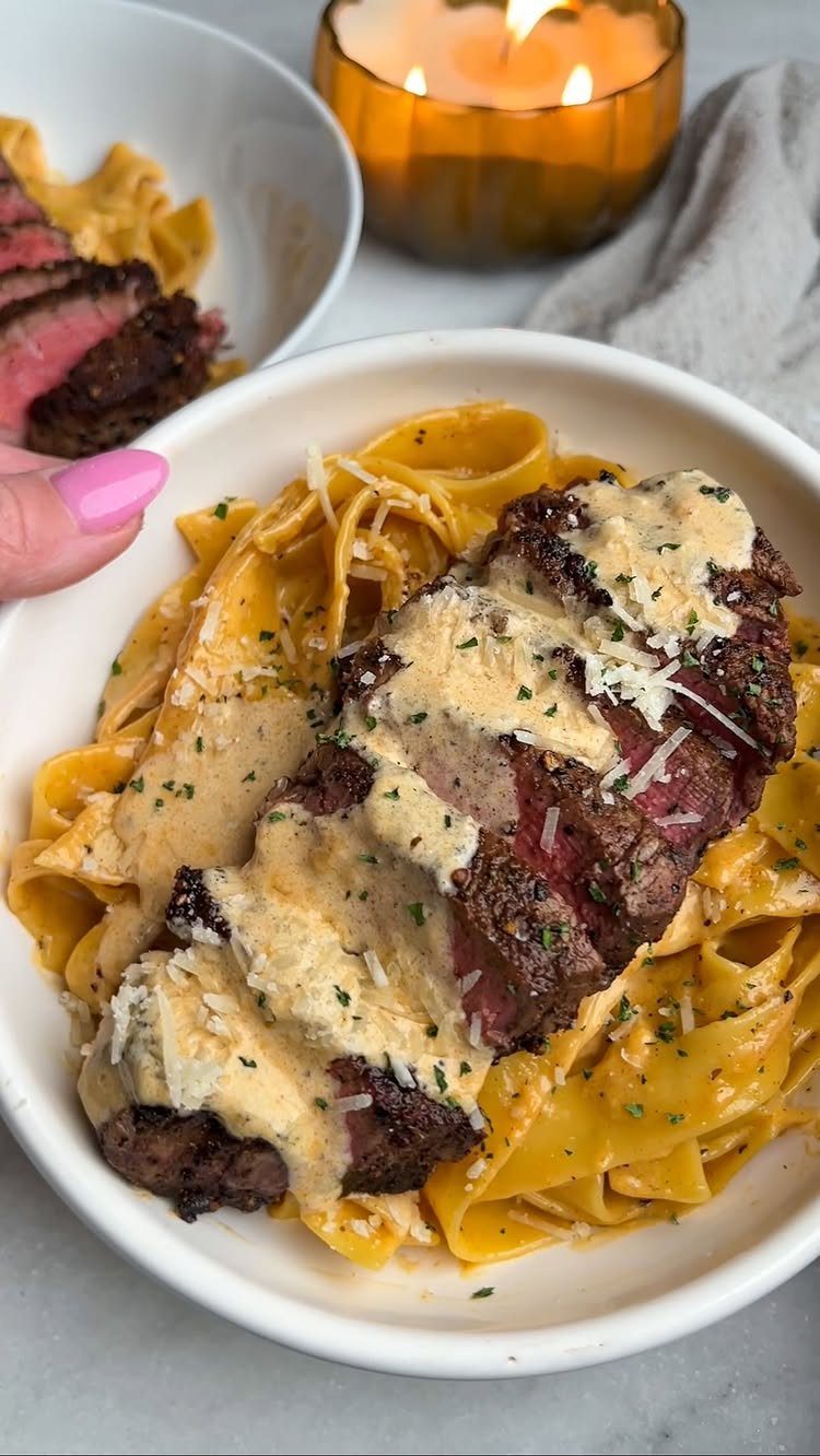 Slices of seared steak with creamy sauce over wide pasta in white bowls