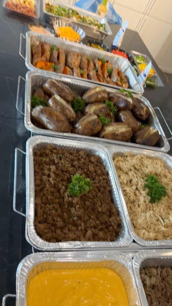 Baked potato bar with trays of potatoes, ground meat, and melted cheese toppings.
