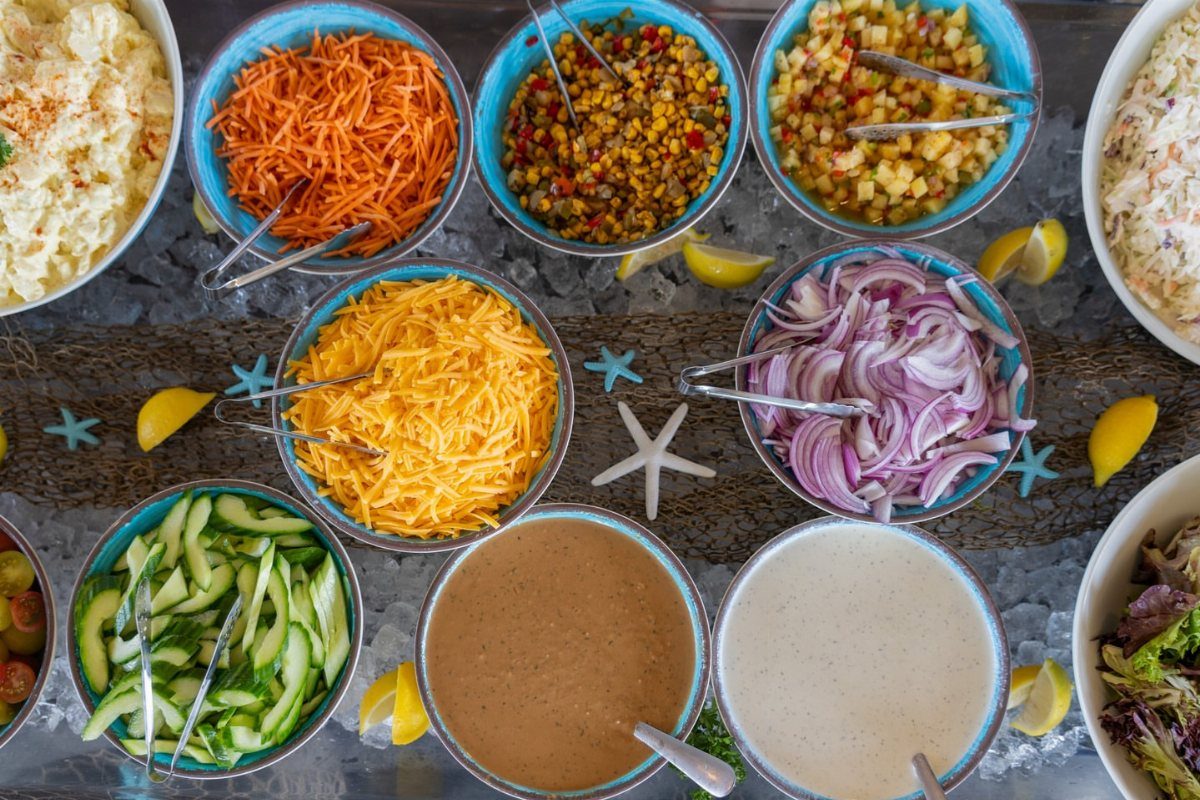Salad bar ingredients in blue bowls on ice with lemon and starfish decorations.