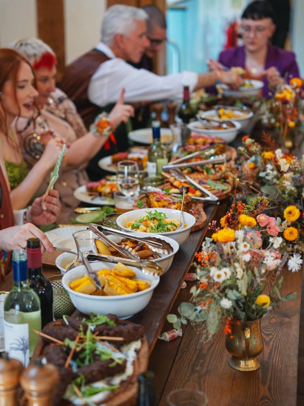Guests sharing large platters of food at a long wooden wedding reception table.