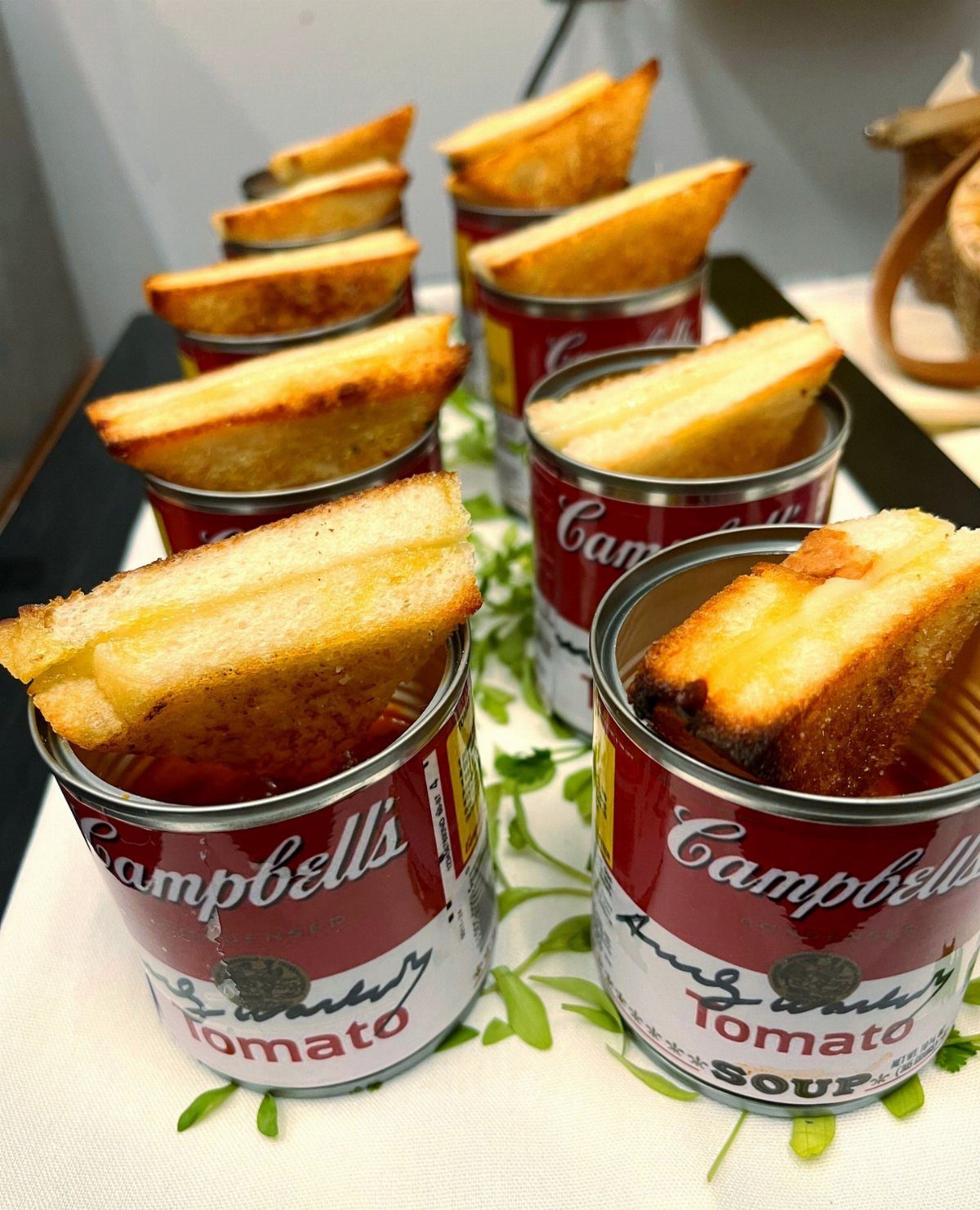 Grilled cheese sandwich wedges served in small cans of tomato soup with microgreens.