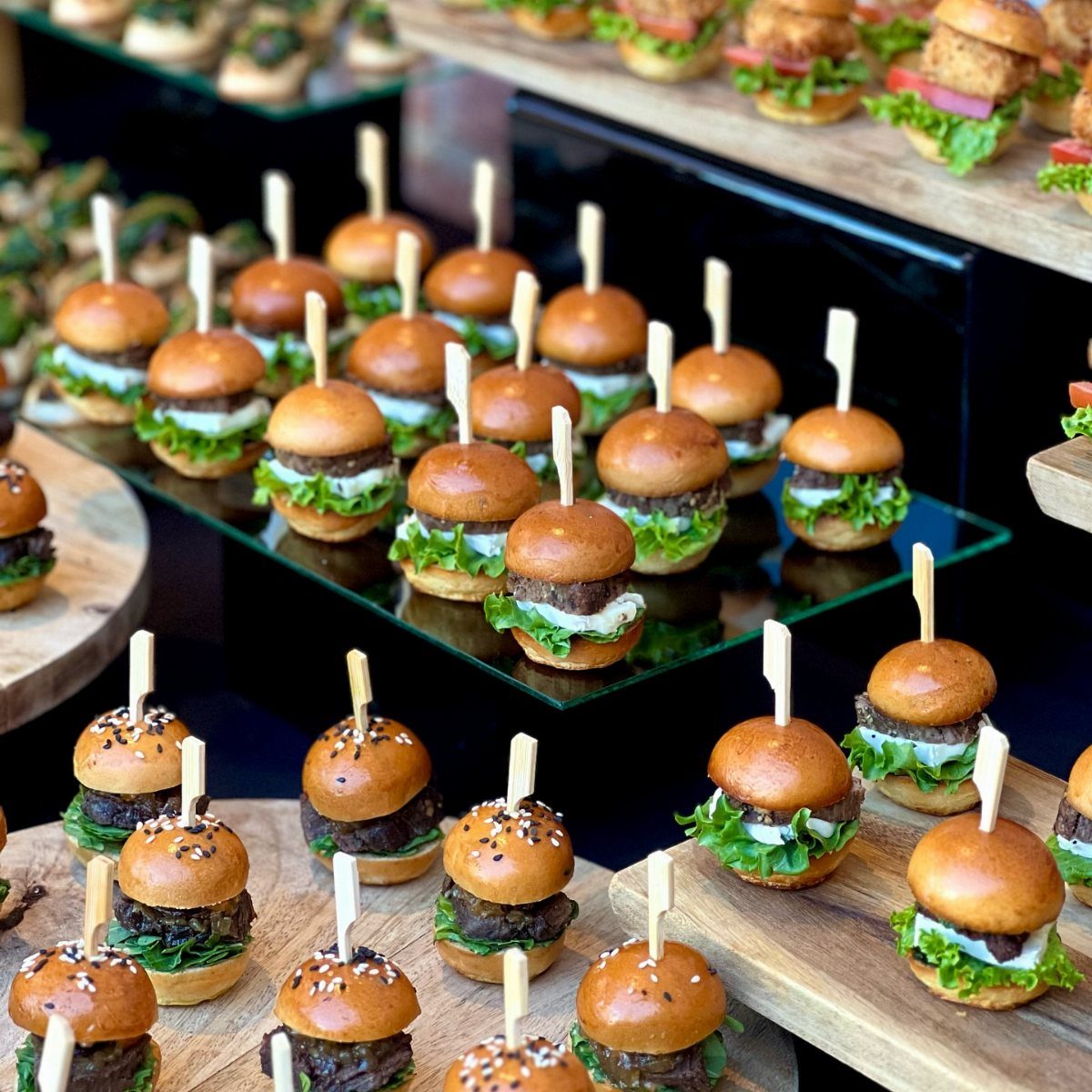 Mini sliders with beef and lettuce on wooden platters for a reception.