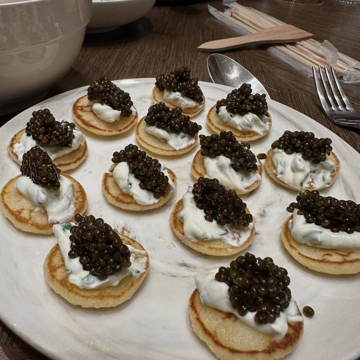 Caviar and cream on small blinis served on a white marble platter.