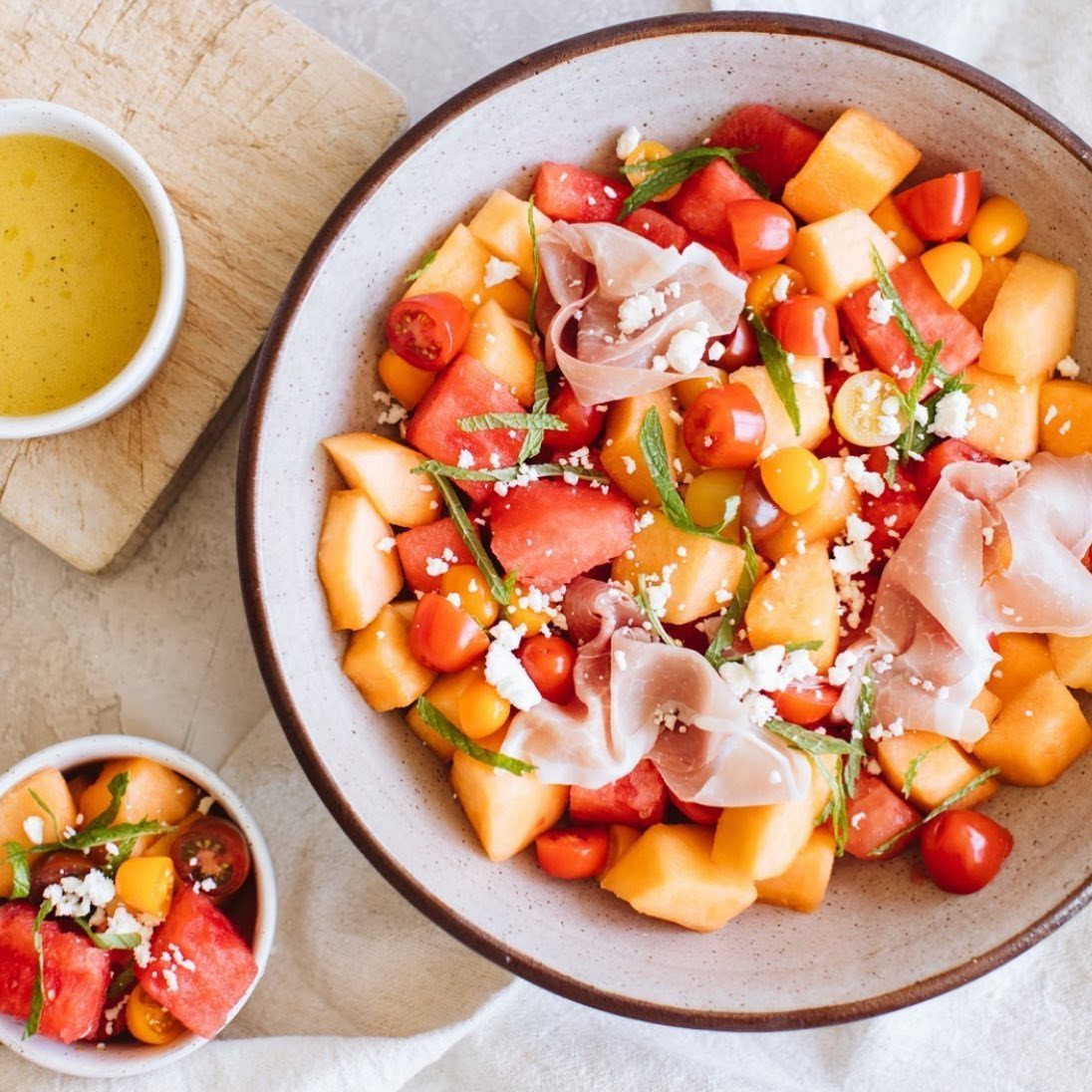 Melon and prosciutto salad with cherry tomatoes and feta in a ceramic bowl