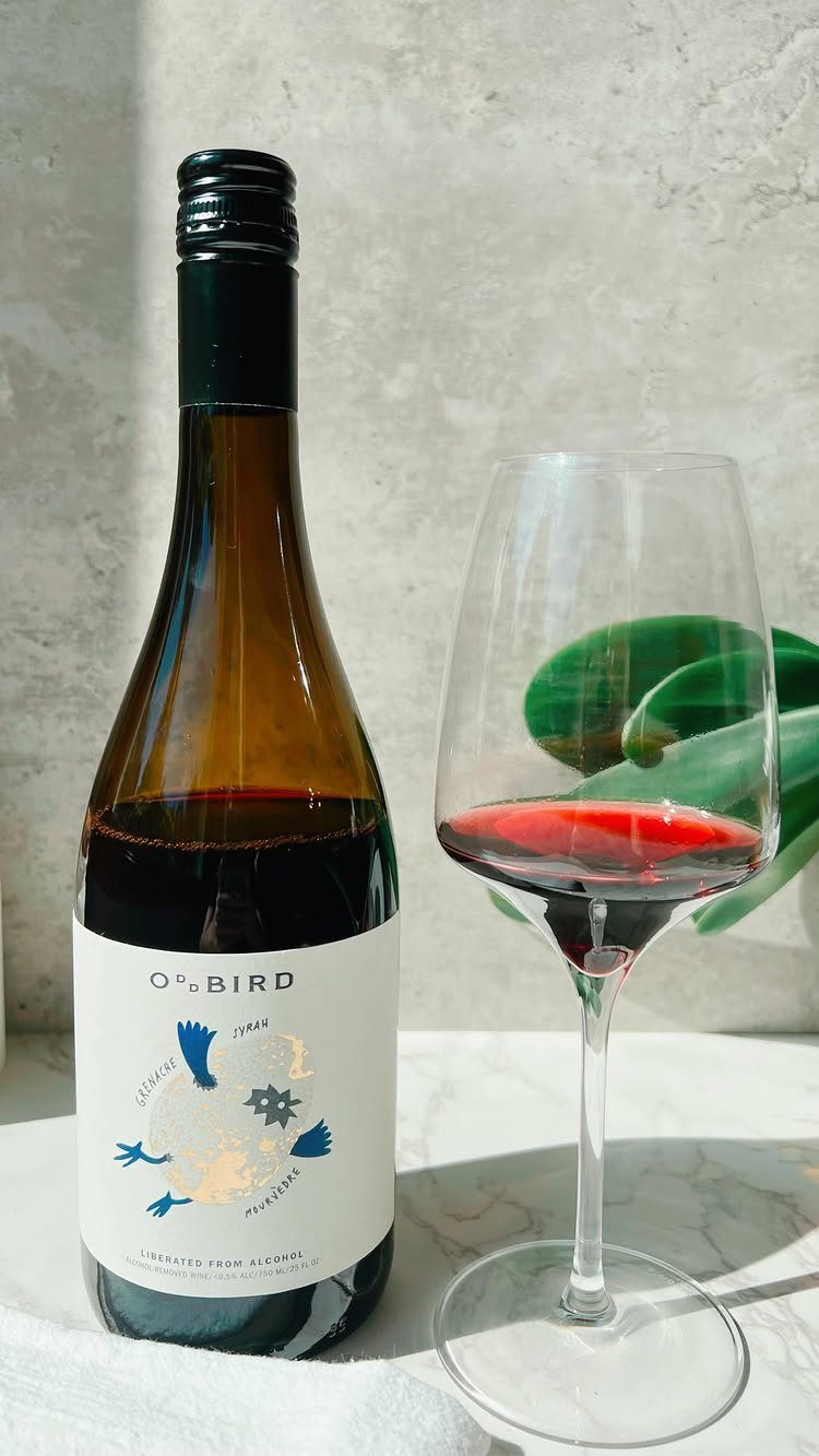 Non-alcoholic red wine bottle and a filled wine glass on marble surface.