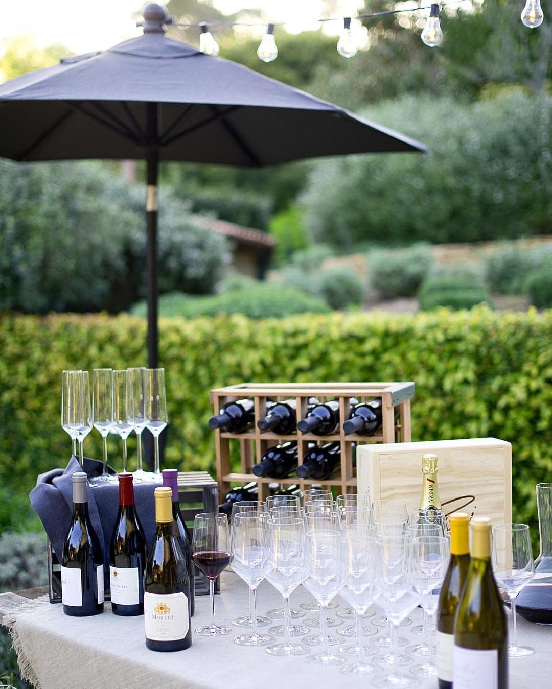 Wine bottles and glasses arranged on a table under a black patio umbrella.