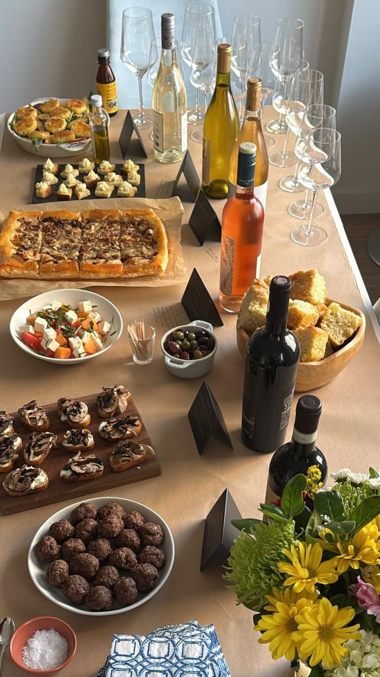 Wine bottles and glasses arranged with various appetizers on a long party table.