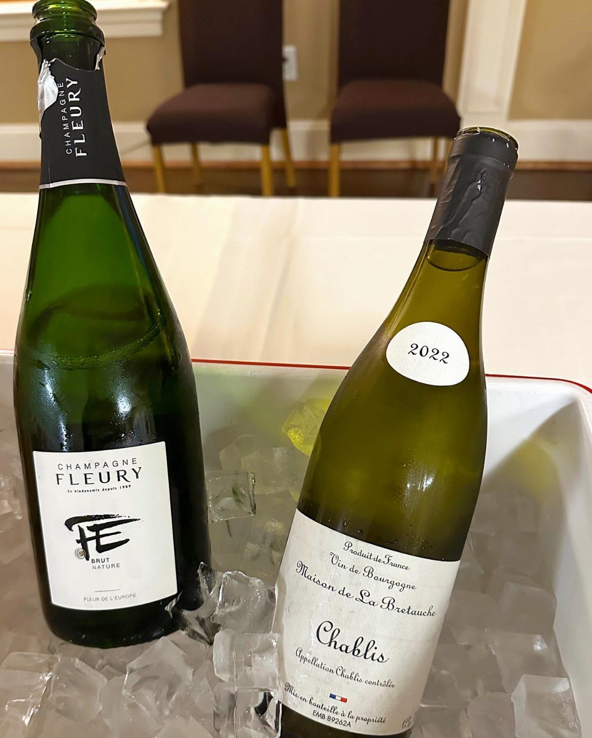 Two bottles of white wine chilling in a white ice bucket on a table.