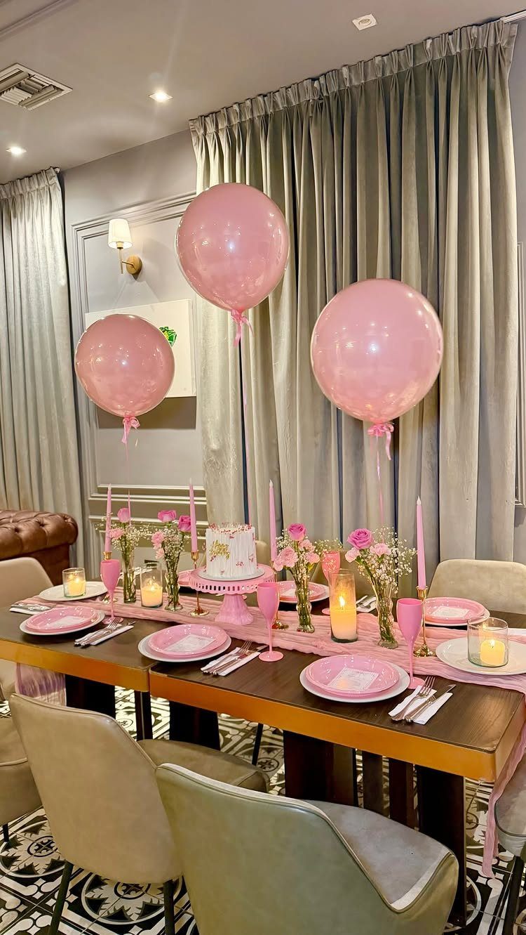 Wooden dining table decorated with pink plates, flowers, and large pink balloons.