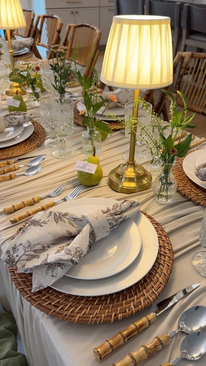 Dining table set with white plates, woven chargers, bamboo cutlery, and glowing lamps.
