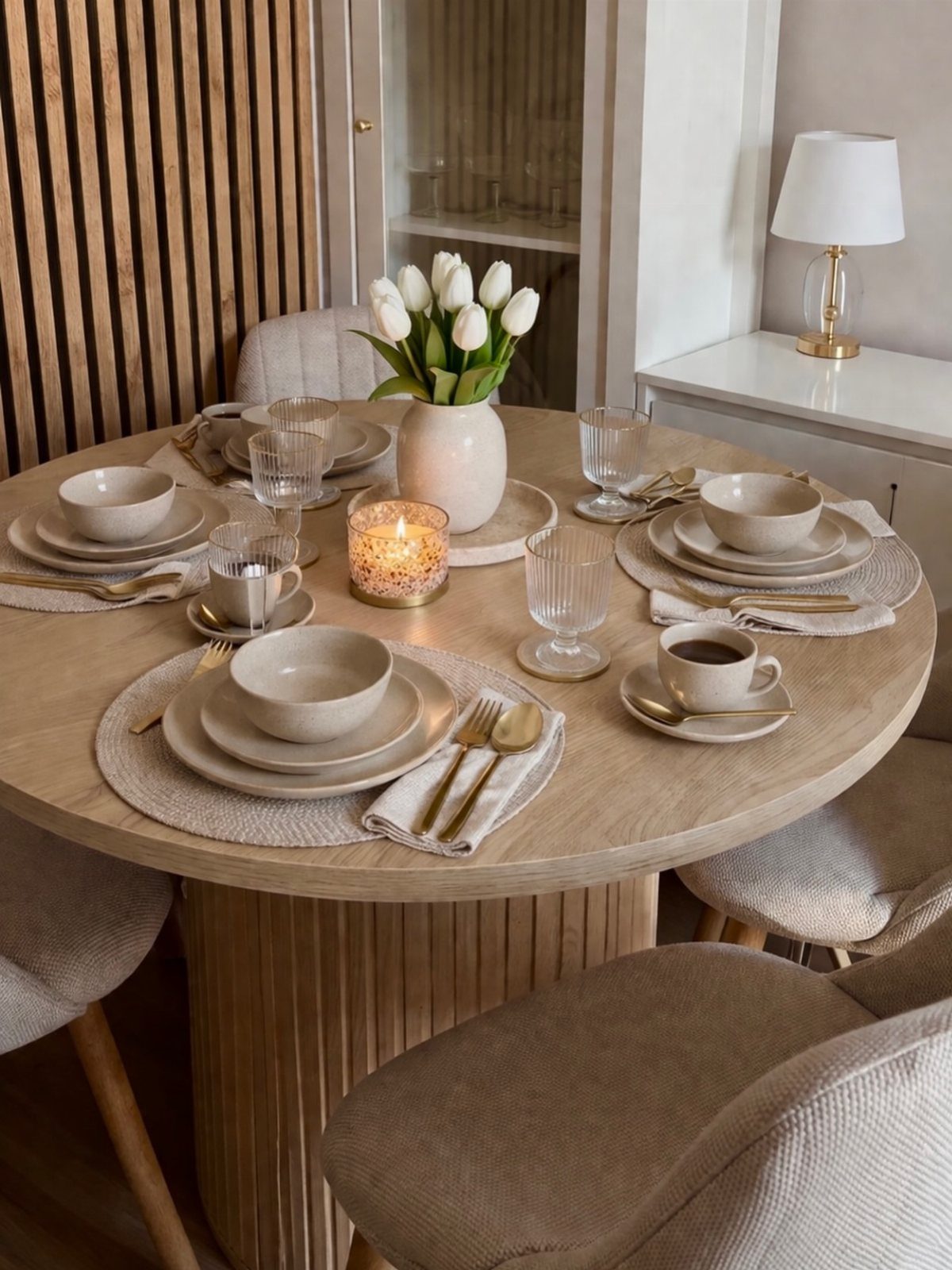 Neutral table setting on a round wooden table with white tulips and lit candle.