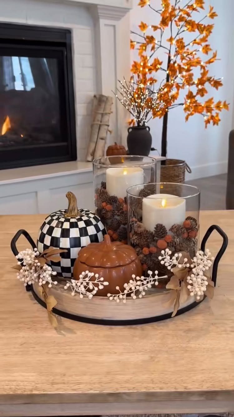 Autumn centerpiece on a wooden table with pumpkins, candles, and orange leaves.